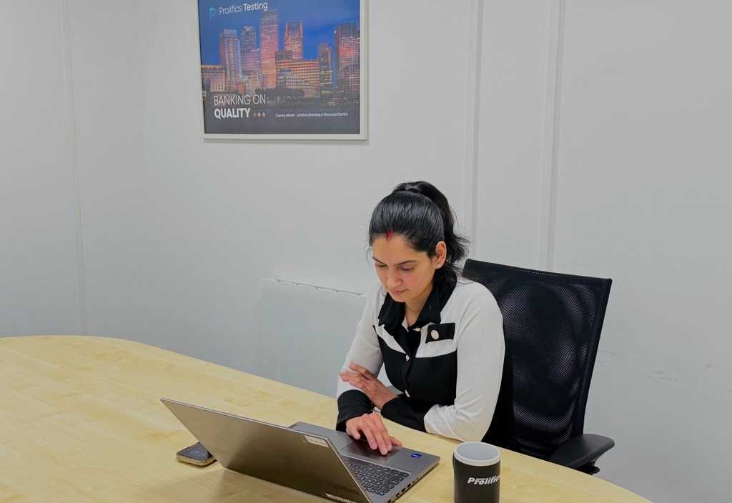 A woman working on a laptop at a wooden table in an office