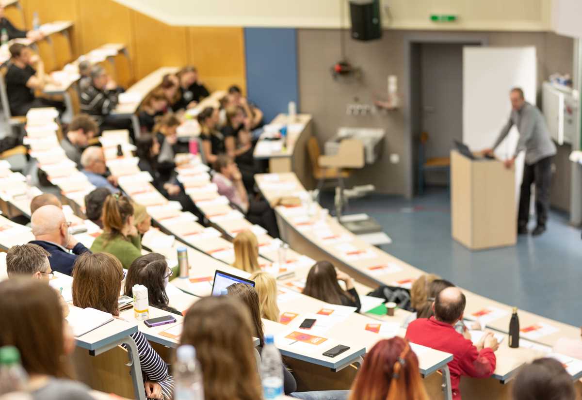 A university classroom filled with students, with a professor leading the session at the front