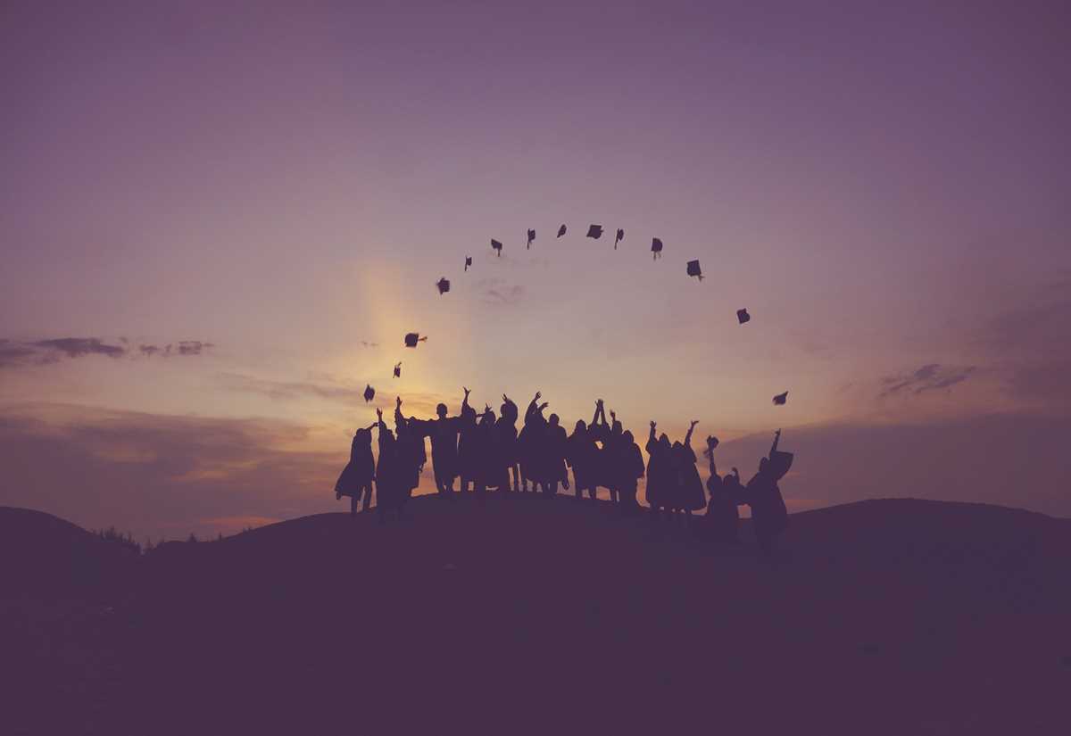 University students celebrating their achievement by tossing graduation hats into the air against a scenic horizon
